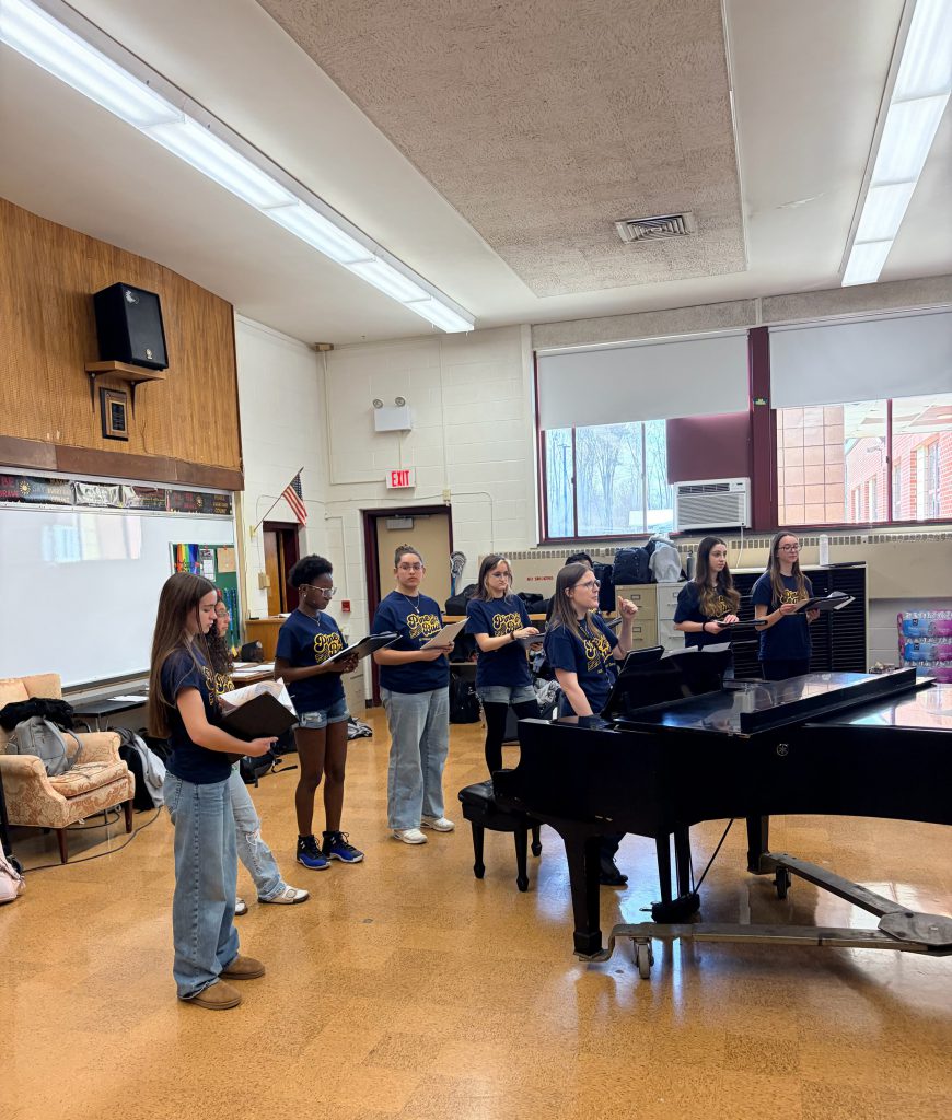 A group of students standing around a piano singing.