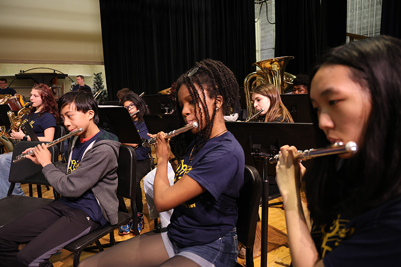 A line of high school and middle school students playing flutes.