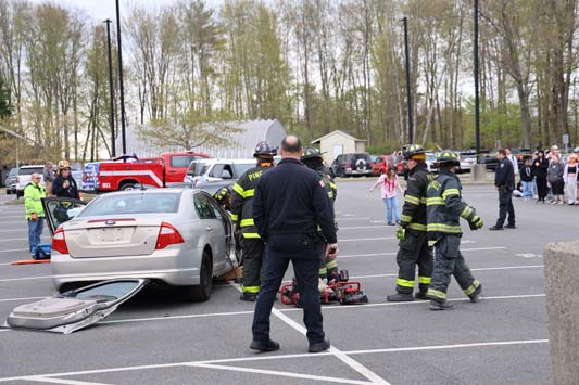 A crashed car in a mock demonstration. There are firefighters all around.