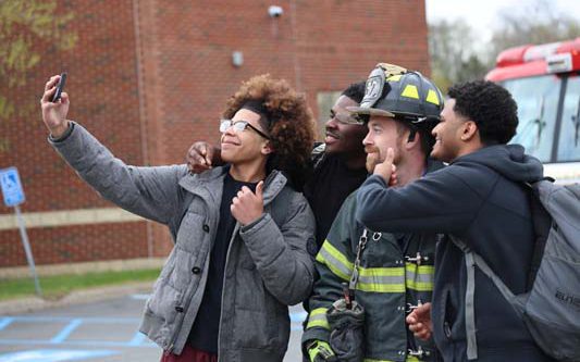 Three high school kids take a selfie with a firefighter.