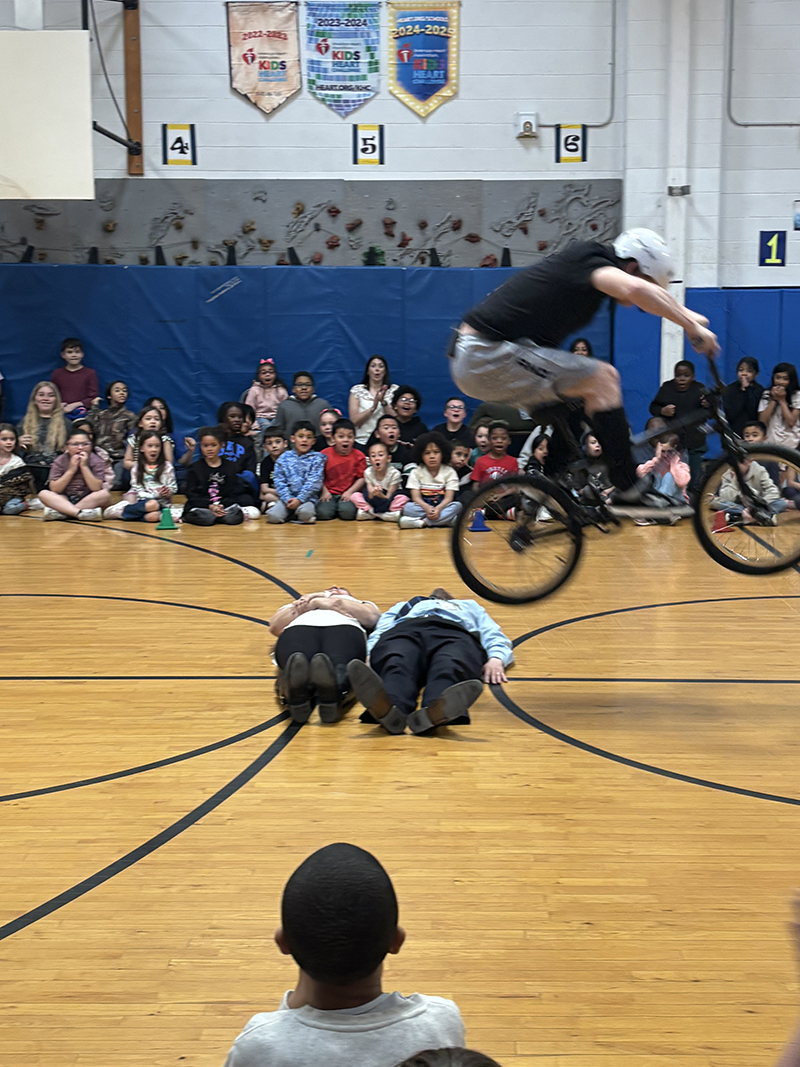 A man on a bicycle jumps over two people lying on the ground.