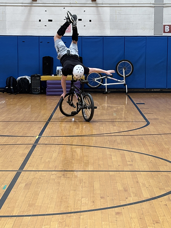 A man rides a bicycle upside down, with his arms out straight and his legs up in the air.