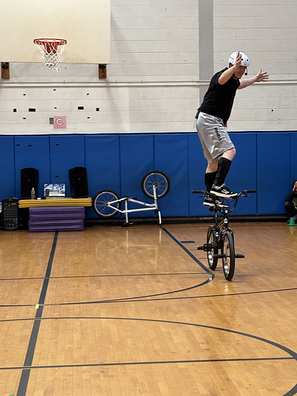A man stands on the seat of a bicycle while it moves.