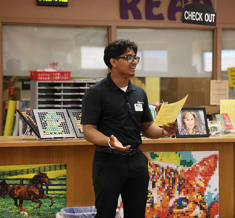A young man stands in front f a group of 8th grade kids, talking about his job.