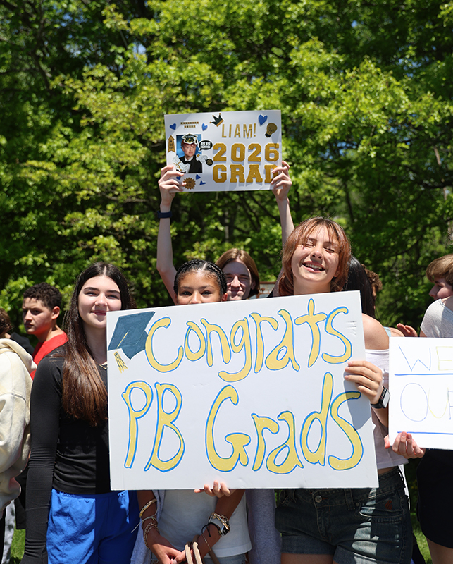 Middle school kids stand with signs wishing good luck to graduates.