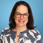A woman smiles. she has shoulder-length dark hair and is wearing glasses.