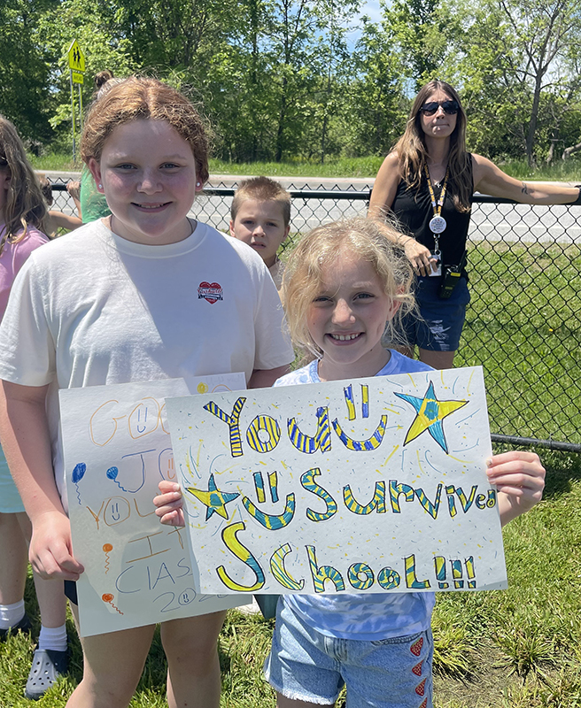 Two elementary girls with a sign that says You survived school.
