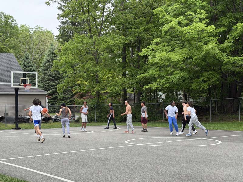 A group of high school kids play basketball on an outside basketball court.