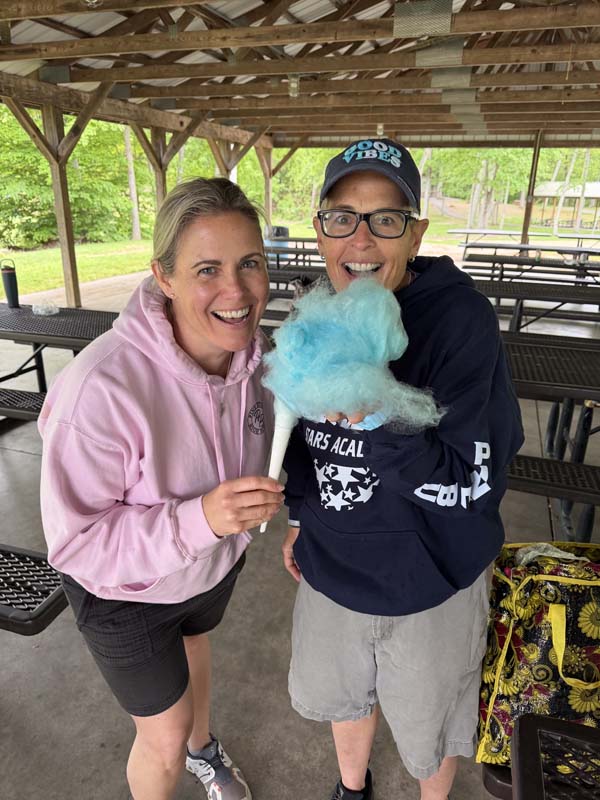 Two women smile as they look to eat bright blue cotton candy.