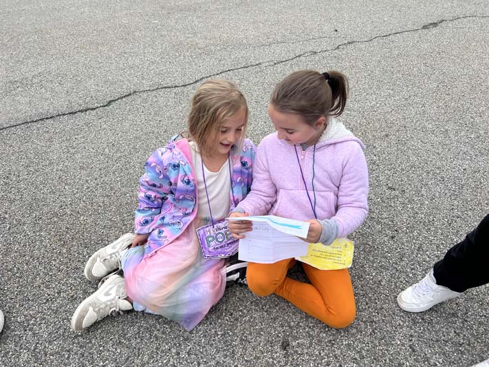 Two girls sit outside. One reads a poem to the other.