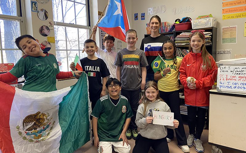 Seven elementary students stand with different flags as they celebrate diversity day.