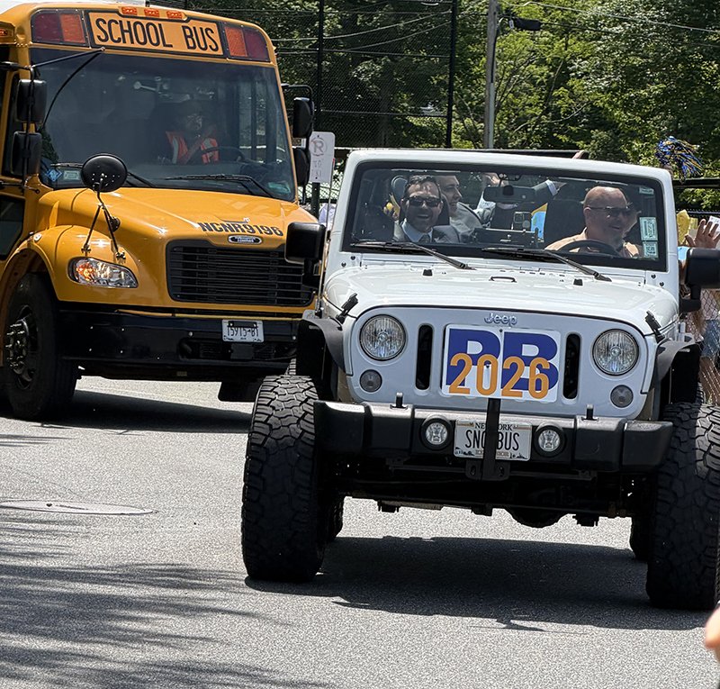 A white Jeep with four people in it waving. A sign on the front says PB 2026