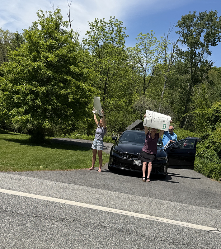 A few people hold up signs for Nessa as a bus parade goes by.