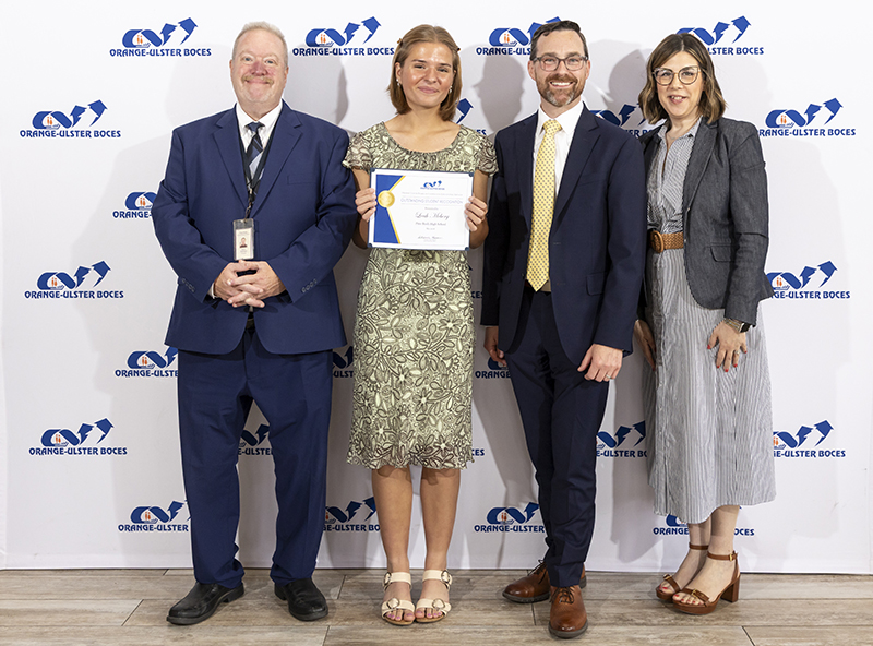 Three adults dressed in suits and dresses stand with a young woman holding a certificate.