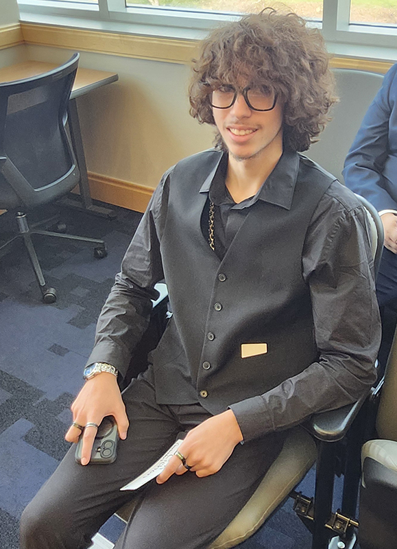 A young man sits in a chair and smiles.