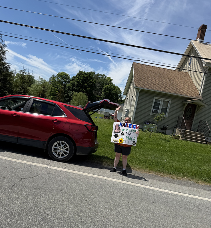A woman stands on the side of the road with a sign of support for a high school kid.