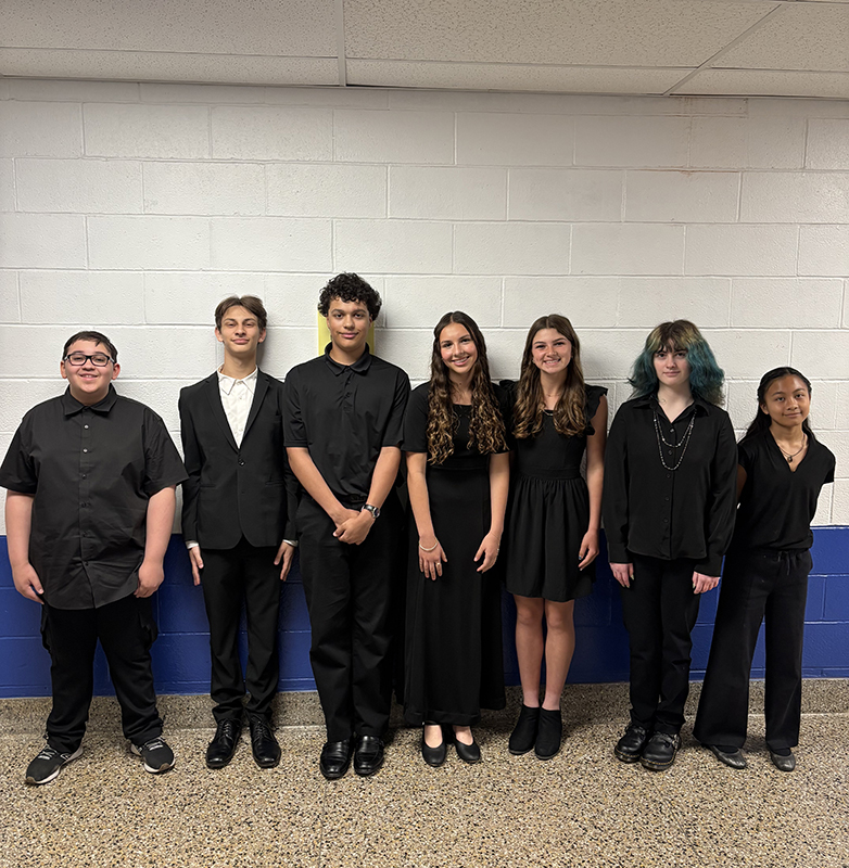 Seven middle school and high school students, all dressed in black, stand together before a concert.