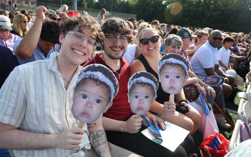 Three people sit in a row and hold up little cardboard pictures of a baby.
