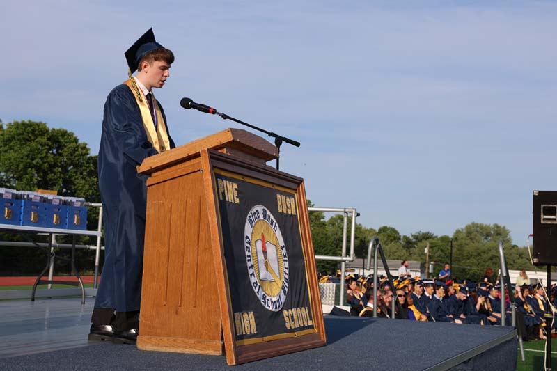 A young man wearing a blue cap and gown stands at a podium.