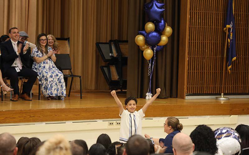 A fifth-grade students stands and throws his arms up with fists held high.