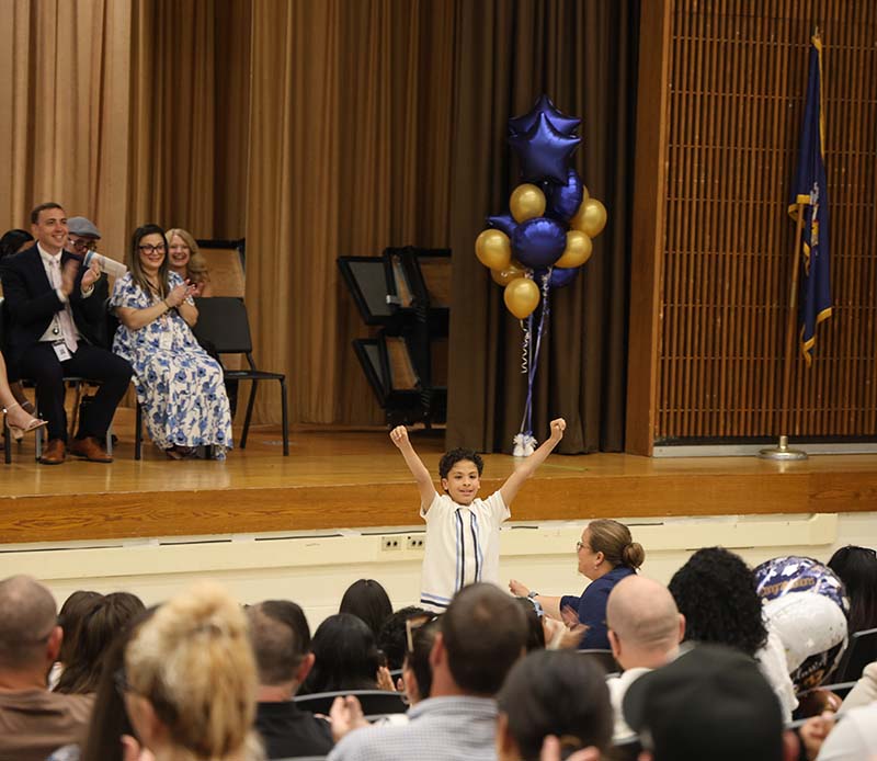 A fifth-grade students stands and throws his arms up with fists held high.