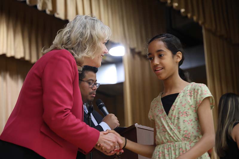 A fifth-grade girl smiles and shakes hands with a woman.
