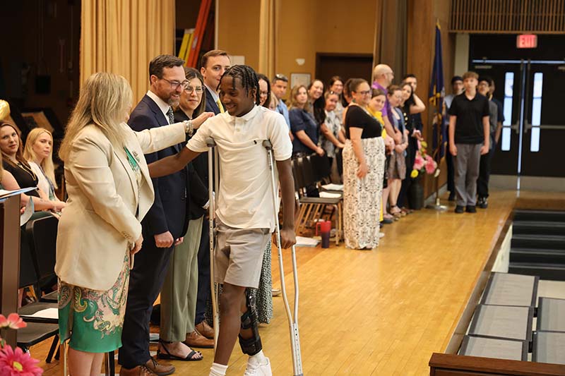 Eighth-grade kids walk across a stage with adults looking on.