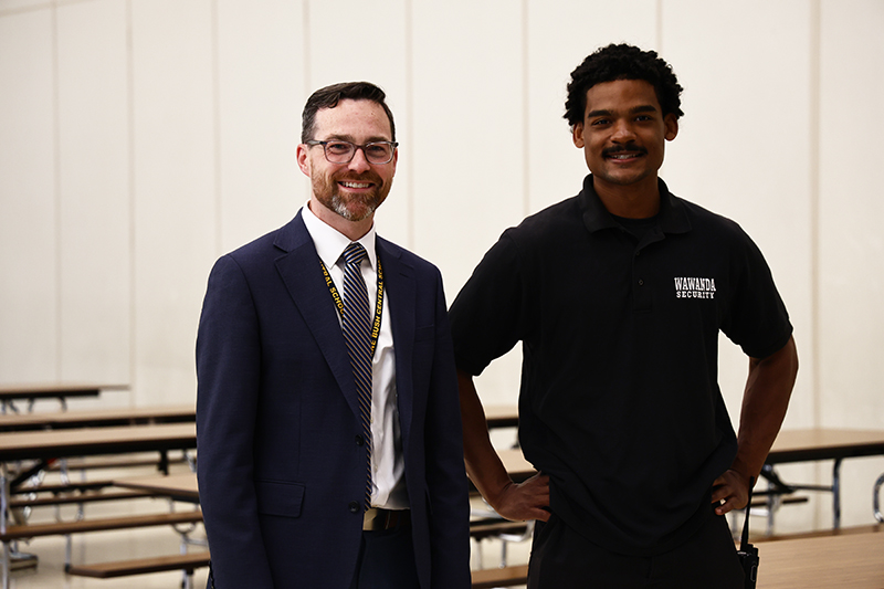 Two men stand together smiling.