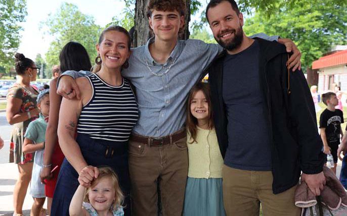 A young man has his arms around a man and a woman. There are two little girls there too. All are smiling.