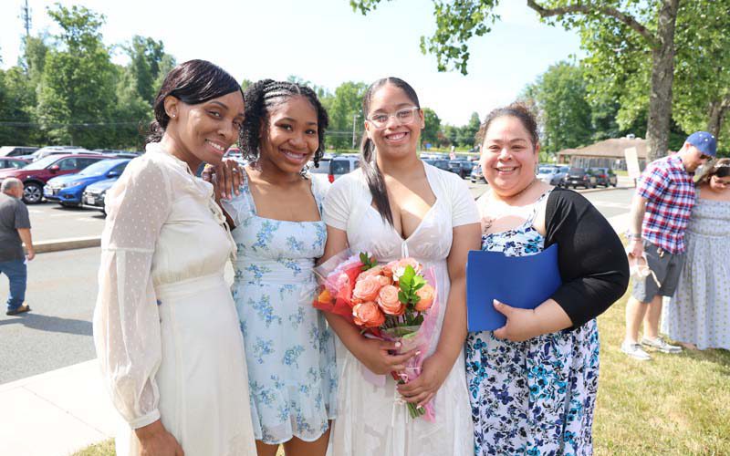 Two women flank two eighth-grade girls who are holding flowers. All are smiling.