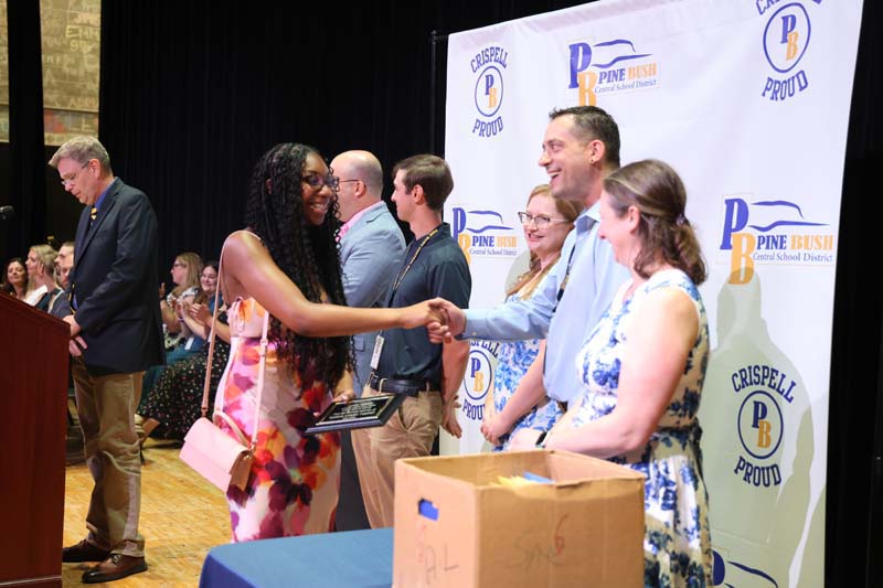 An eighth-grade girl shakes hands with a man. Others are around and all are smiling.