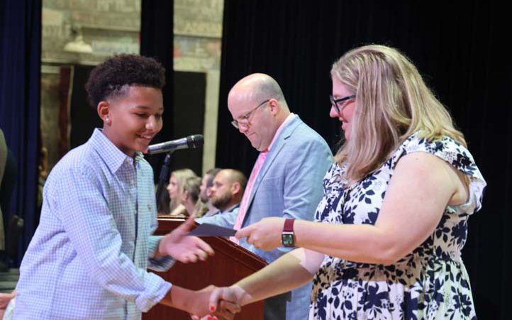 An eighth-grade boy shakes hands with a woman as he receives his certificate to move up to high school.