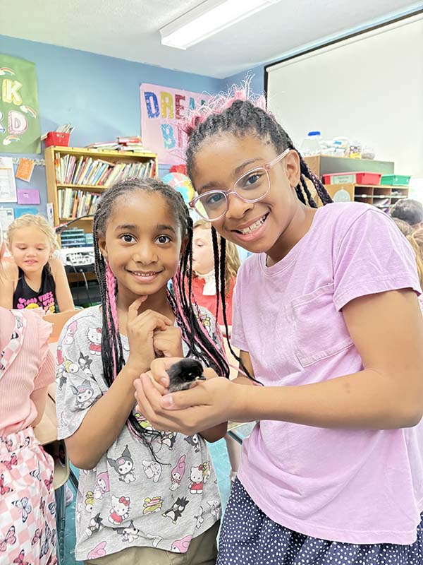 Two fourth-grade girls smile as they hold a chick.