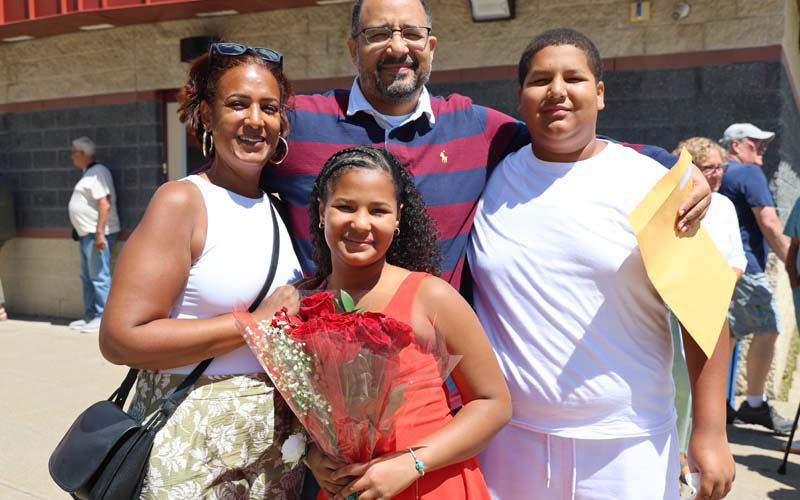 A family of four people stand and smile.