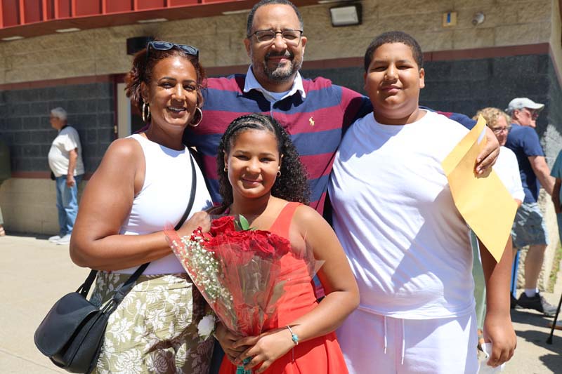 A family of four people stand and smile.