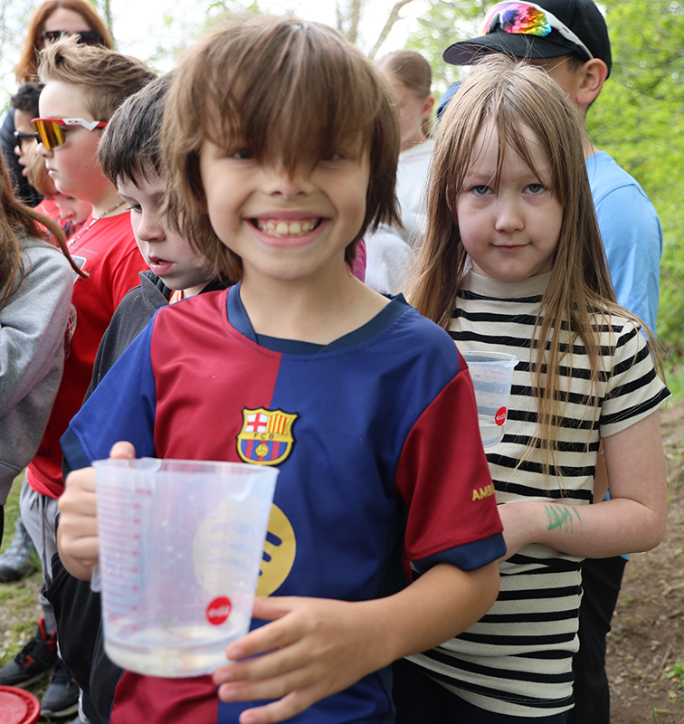 A third-grade boy smiles broadly as he holds a cup with a fish in it.