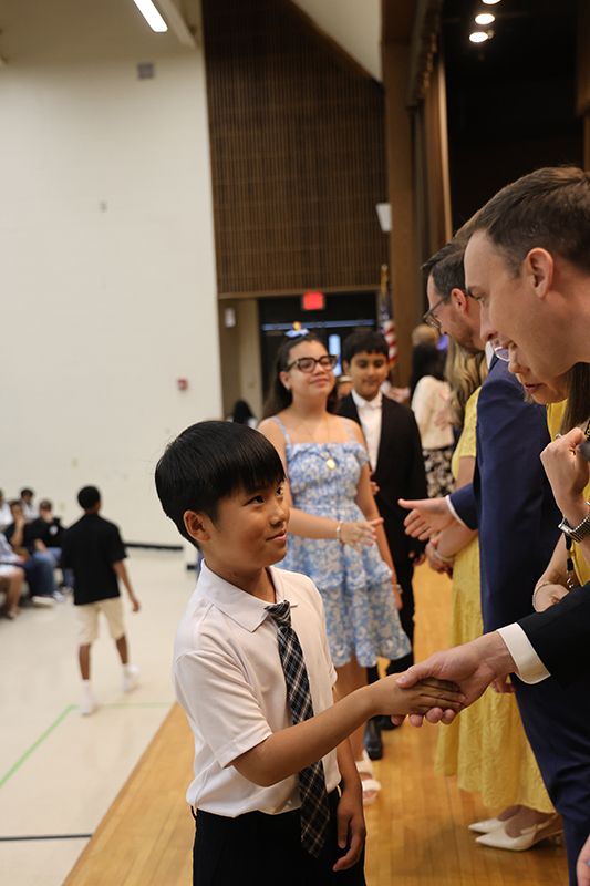 A fifth-grade boy looks up at a man who is smiling at him. They are shaking hands.