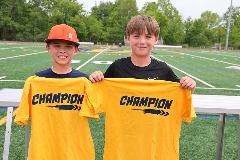 Two fifth-grade boys hold up yellow tshirts that say champion.
