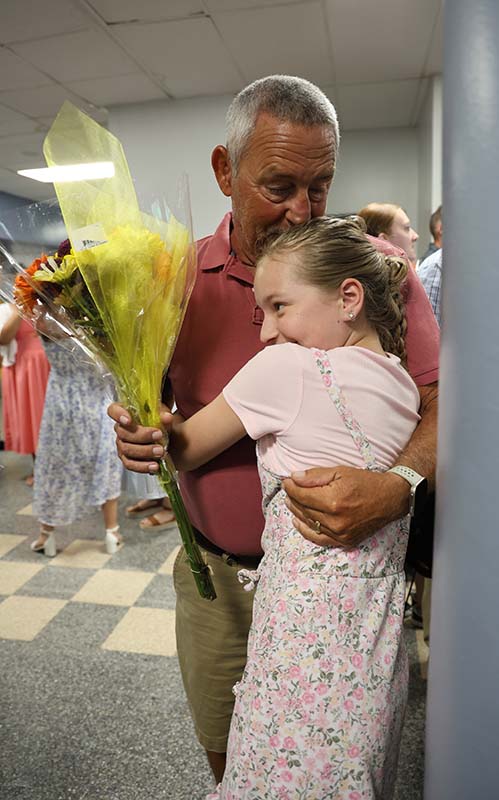 A fifth-grade girl hugs a man who is holding flowers for her.