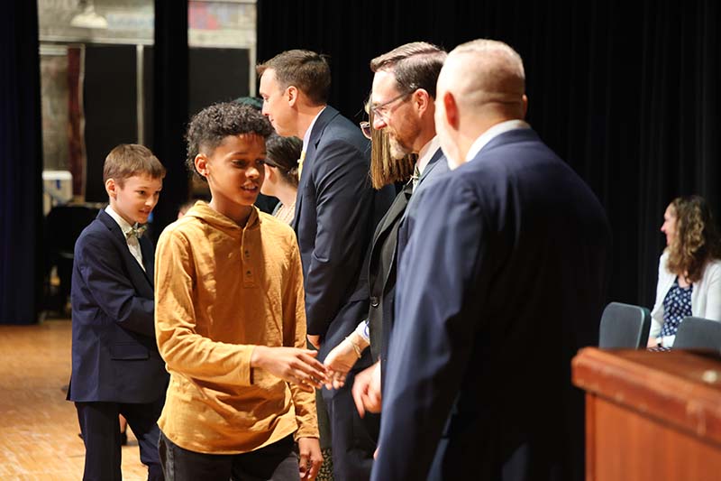 A fifth-grade boy shakes hands with a group of adults.