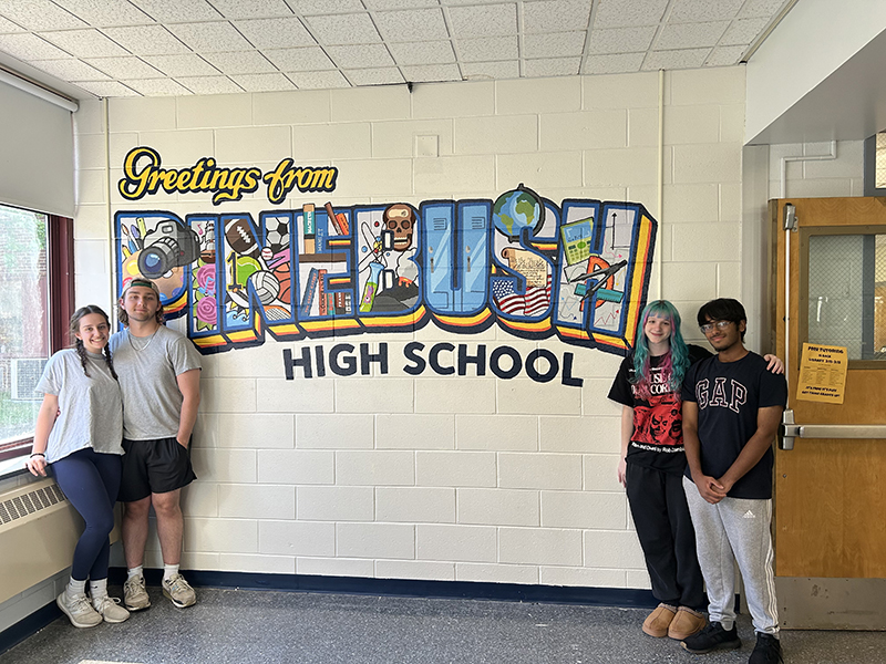 A multi-colored mural on a beige wall that says Greetings from PineBush High School.