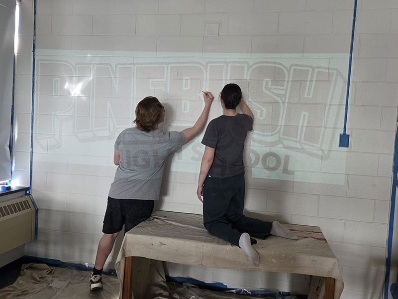 Two high school kids work on what will be a mural on a high school wall.