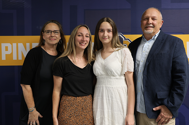 Three adults and a high school senior girl stand together smiling.