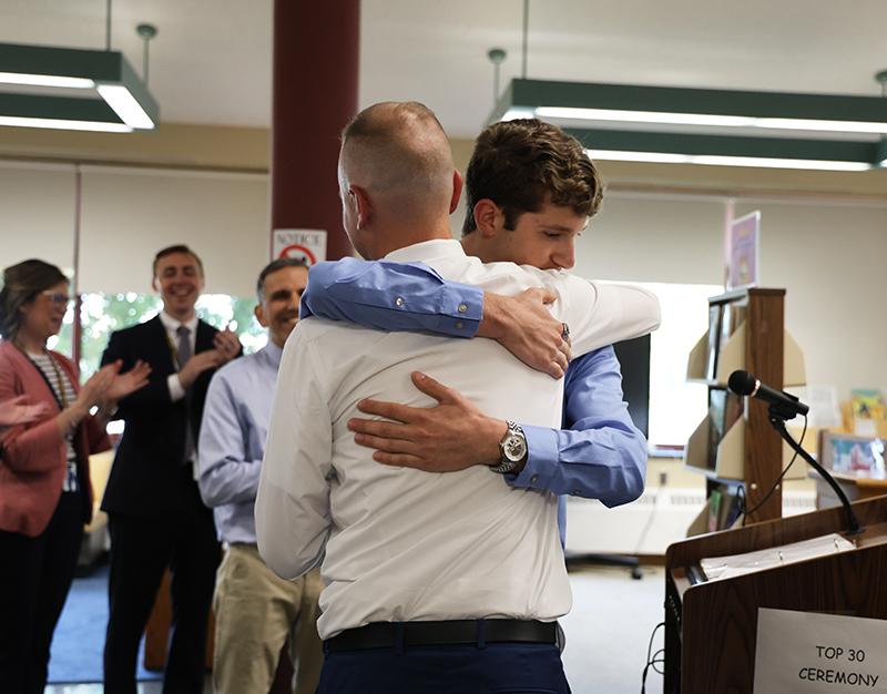 A young man hugs a man while others look on and clap.