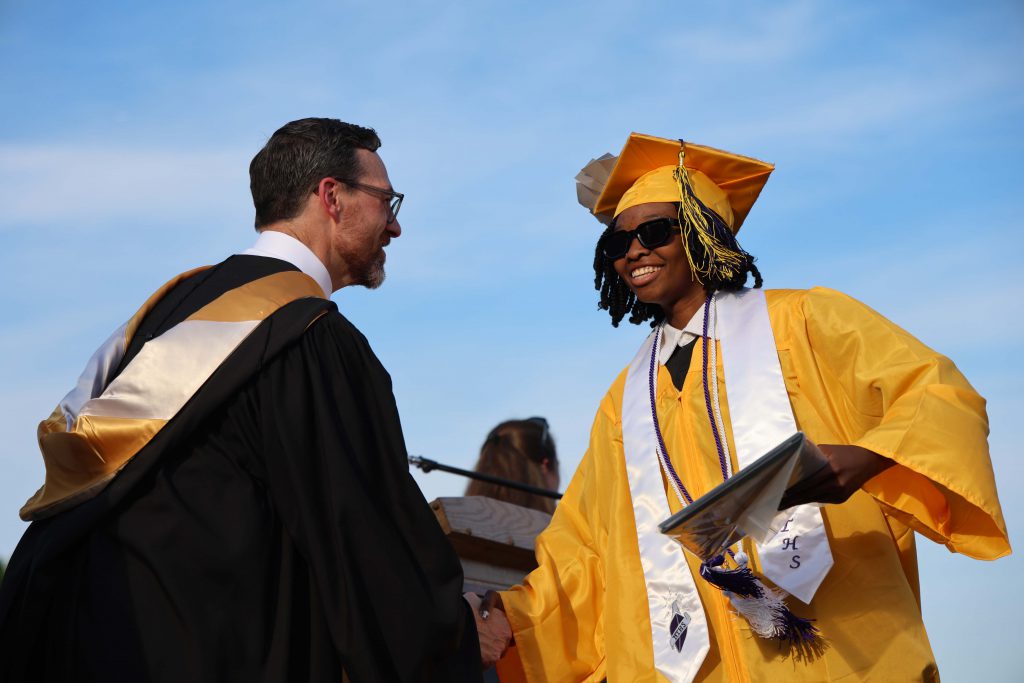 A young man in a gold cap and gown shakes hands with a man in a black gown.