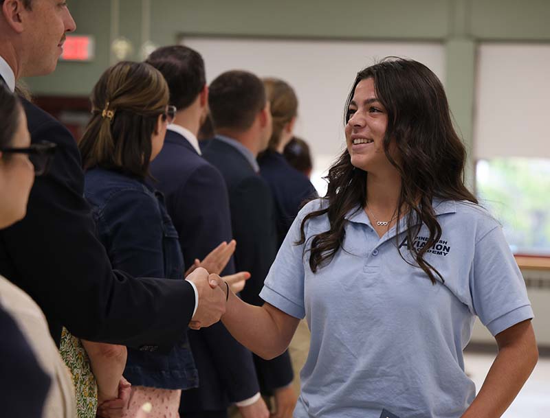 A girl with long dark hair shakes hands with a man.
