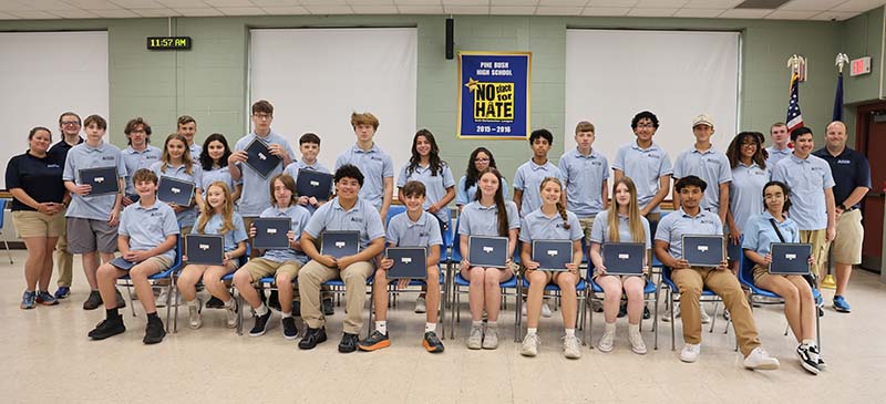 a group of 28 high school kids and three adults stand together. All the kids have light blue polo shirts on and the adults have dark blue.