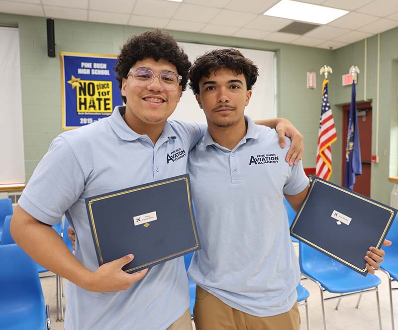 Two high school boys have an arm around each other and show their certificates.