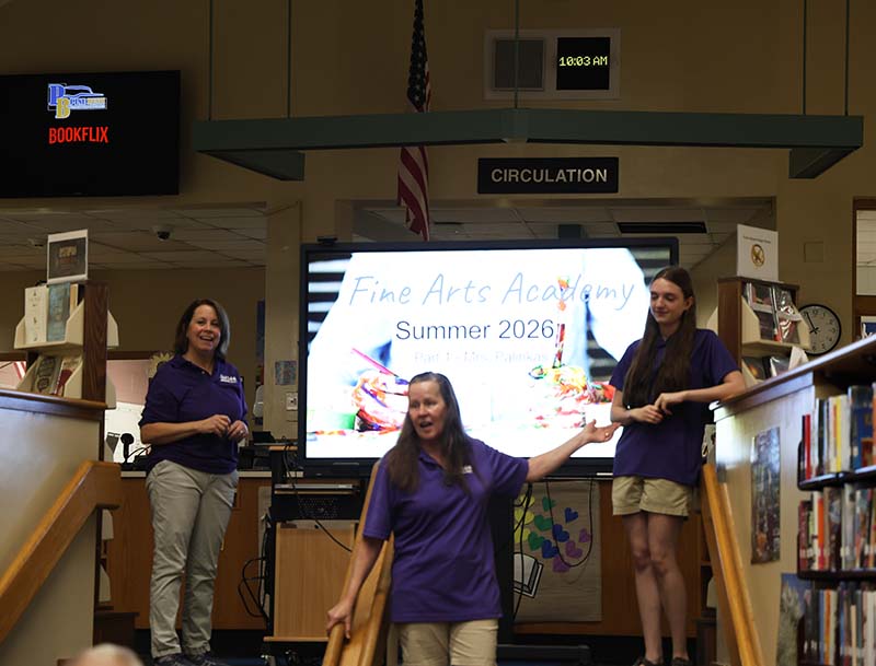 Three teachers stand in front of a board that says Fine Art Academy.