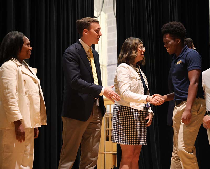 A young man shakes hands with a woman on a stage.